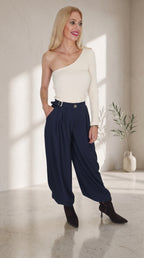 Modelo con top beige de un hombro y manga larga, combinado con pantalón globo azul marino de hebilla lateral.