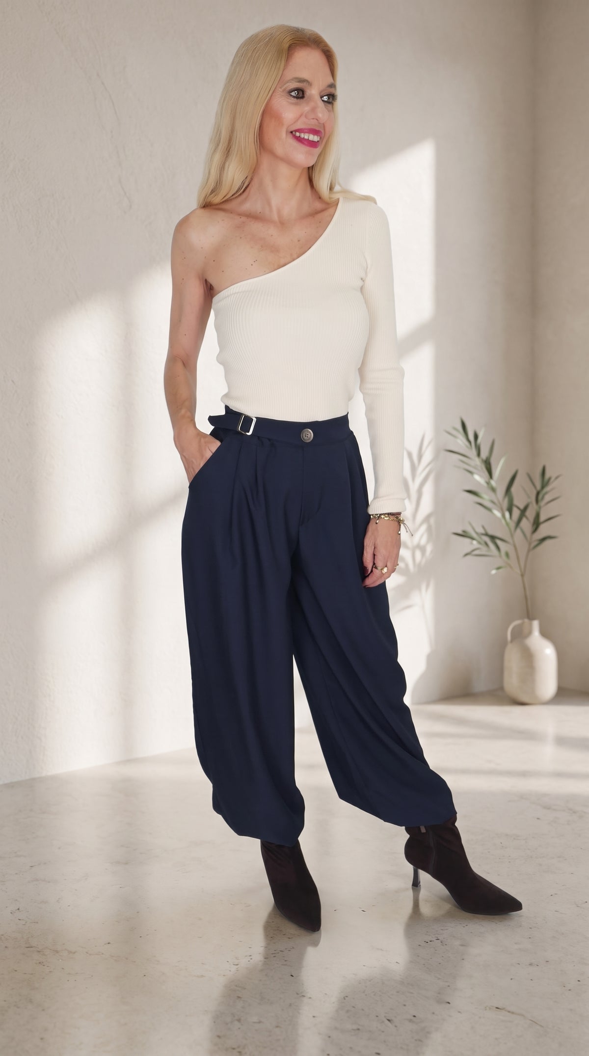 Modelo con top beige de un hombro y manga larga, combinado con pantalón globo azul marino de hebilla lateral.