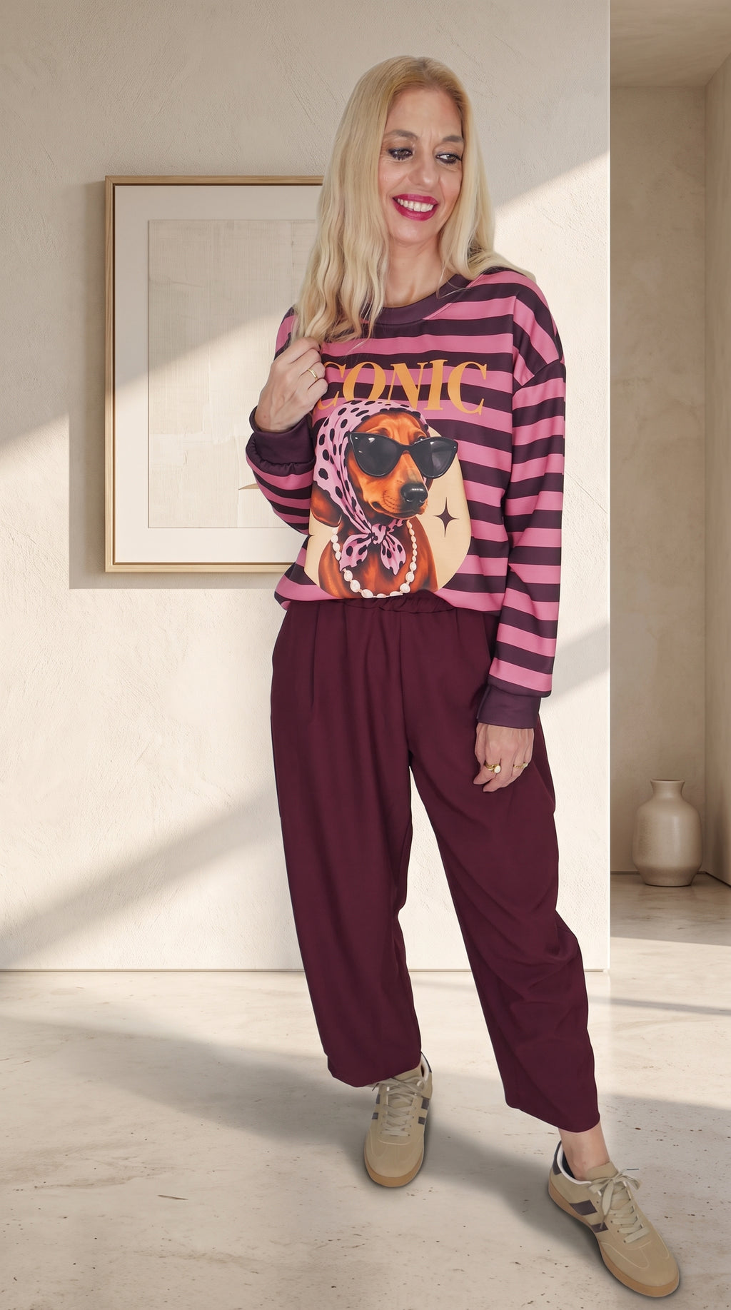 Modelo con sudadera Iconic de rayas rosas y oscuras, estampado de perro con gafas y pantalón burdeos.