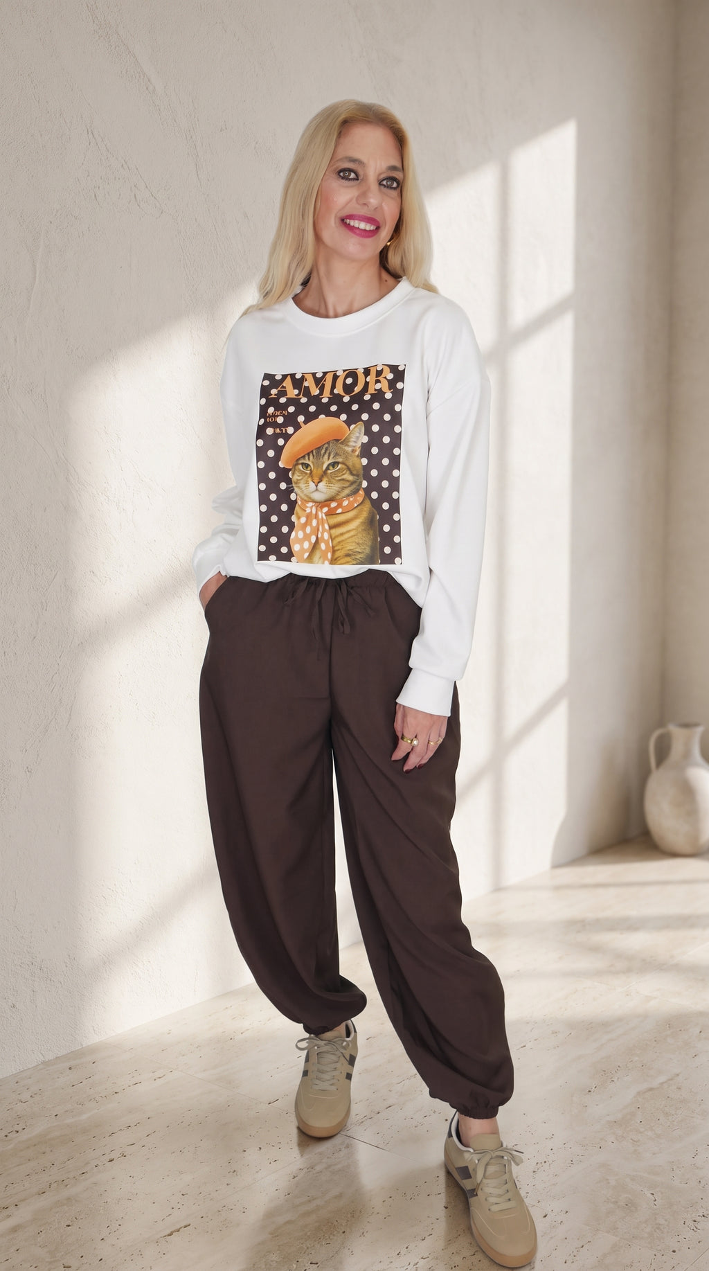 Vista frontal de modelo con sudadera blanca AMOR de estampado de gato y pantalón Track marrón de corte globo.