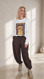 Vista frontal de modelo con sudadera blanca AMOR de estampado de gato y pantalón Track marrón de corte globo.