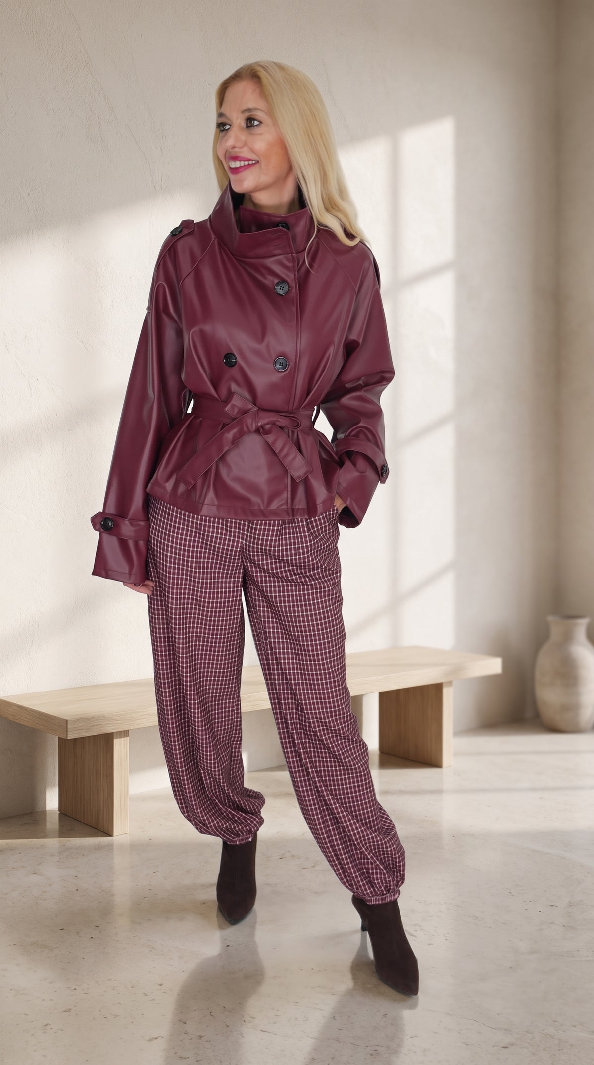 Modelo con trench corto burdeos efecto piel y cinturón, combinado con pantalón balloon de cuadros.