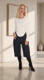 Modelo con camiseta Essential blanca de manga larga, cuello redondo y bajo en pico, combinada con bermudas vaqueras oscuras.